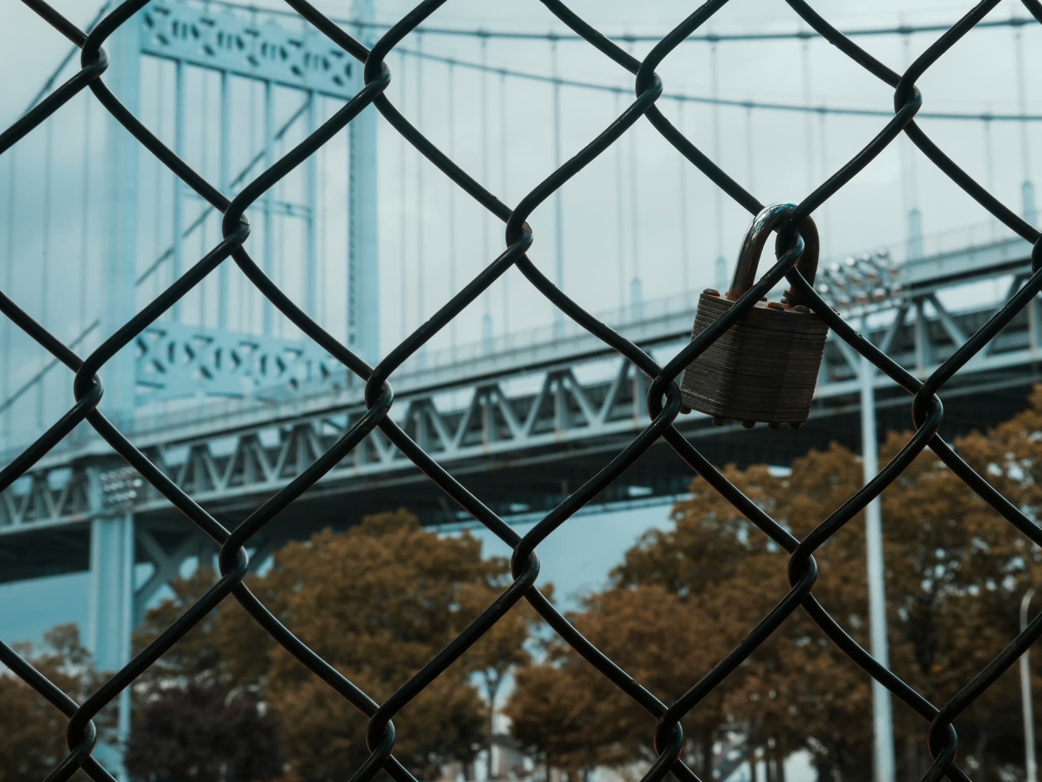 padlock-attached-to-a-chainlink-fence-with-a-bridge-in-the-background