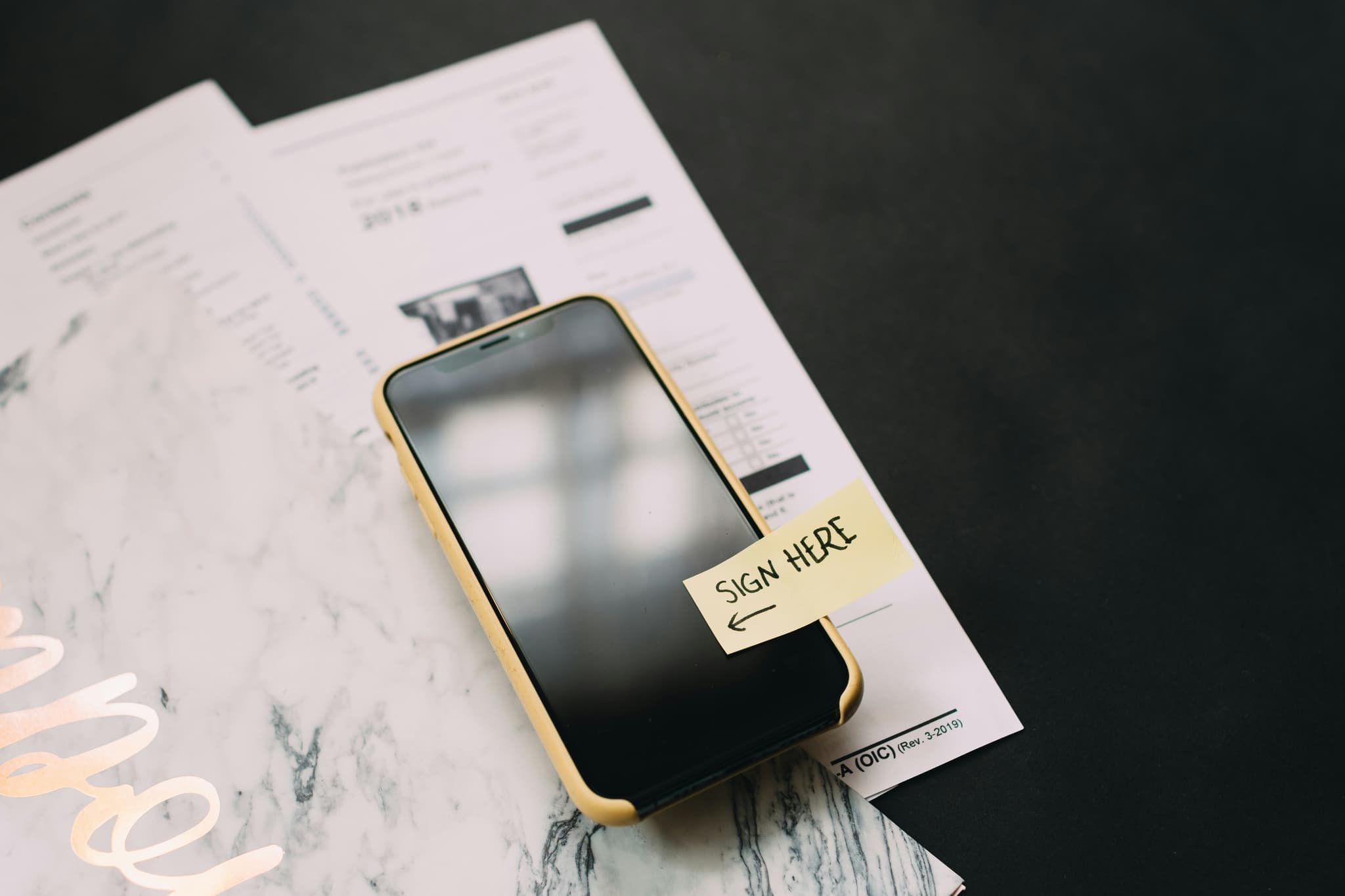 smartphone-with-a-sign-here-sticky-note-on-a-marble-surface-next-to-documents